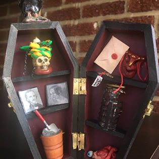 Coffin-shaped box with a raven on top. Inside, various items represent works of Edgar Allan Poe