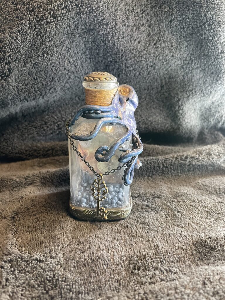 A nautical themed bottle with a blue octopus attached. A small key hangs from the bottle.