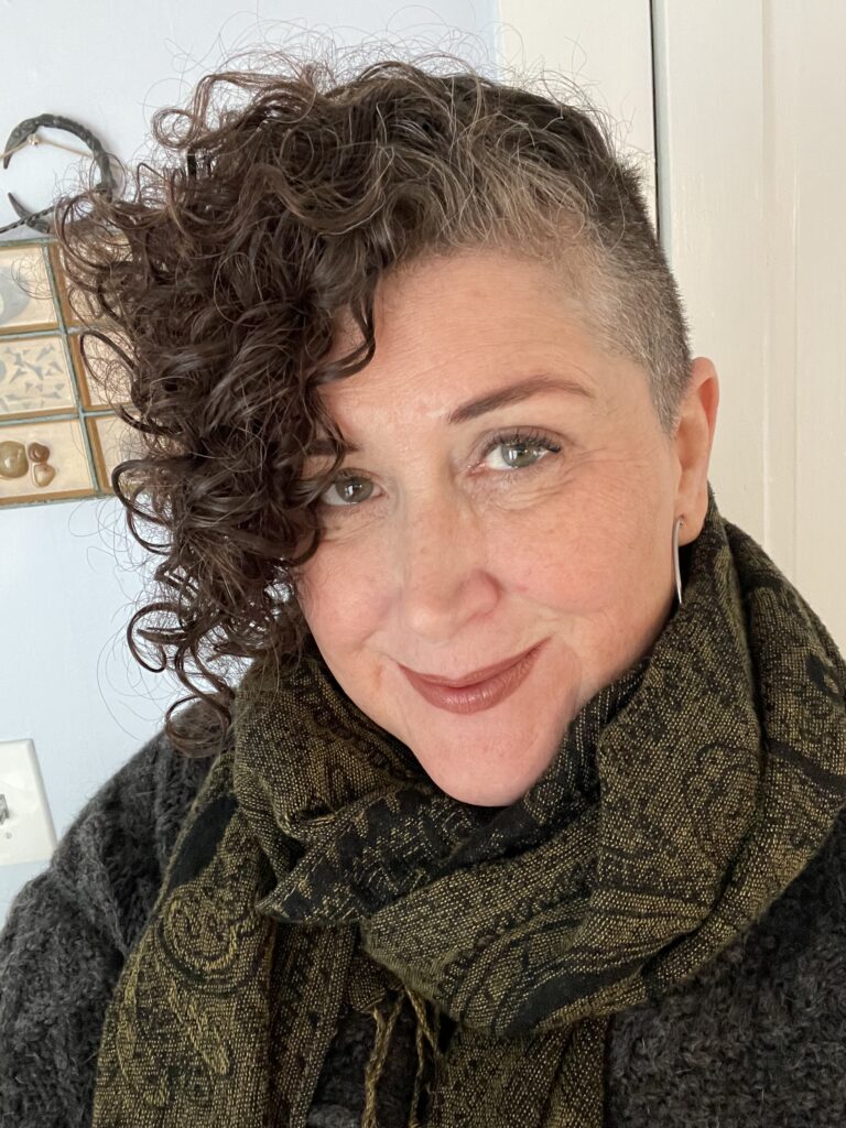 Jennifer Reynolds, white woman with curly hair hsaved on the sides, wearing a green scarf